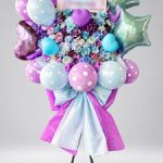 水色と紫のお花に、ハート型・星型・ドット柄のバルーンと大きなリボンを合わせたスタンド花